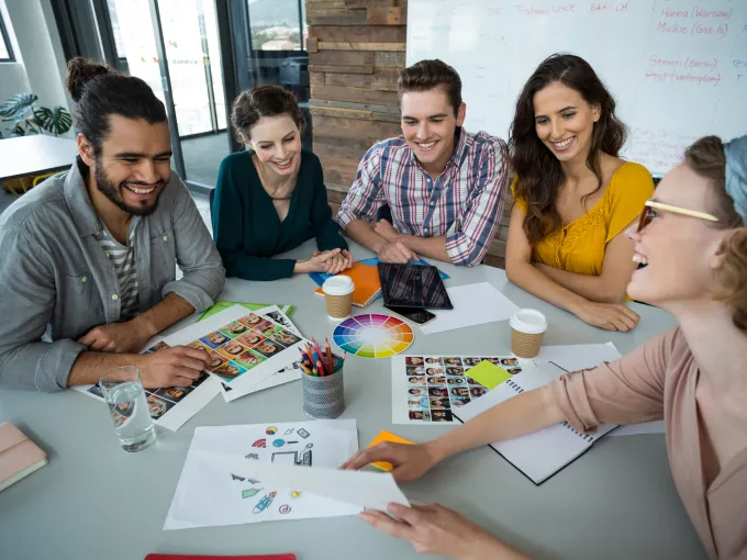 Equipo de diseñadores gráficos reunidos en una mesa colaborando en un proyecto creativo con paletas de colores, bocetos y fotografías.