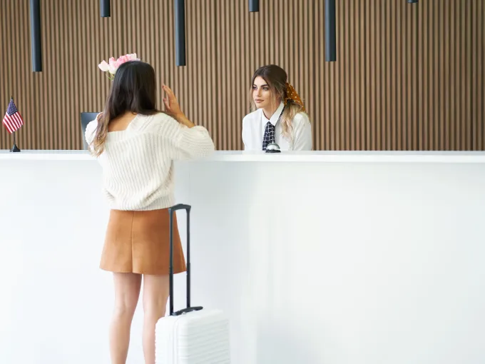 Recepcionista atendiendo a una clienta en el mostrador de un hotel, ejemplo de atención al cliente y comunicación en un entorno internacional.