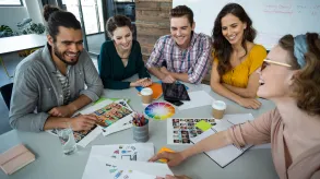 Equipo de diseñadores gráficos reunidos en una mesa colaborando en un proyecto creativo con paletas de colores, bocetos y fotografías.