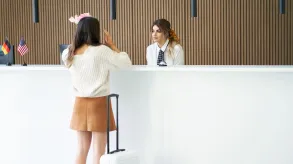 Recepcionista atendiendo a una clienta en el mostrador de un hotel, ejemplo de atención al cliente y comunicación en un entorno internacional.