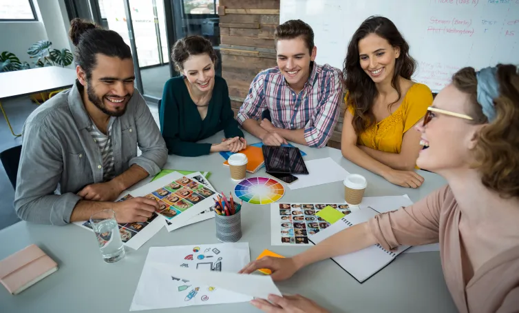 Equipo de diseñadores gráficos reunidos en una mesa colaborando en un proyecto creativo con paletas de colores, bocetos y fotografías.