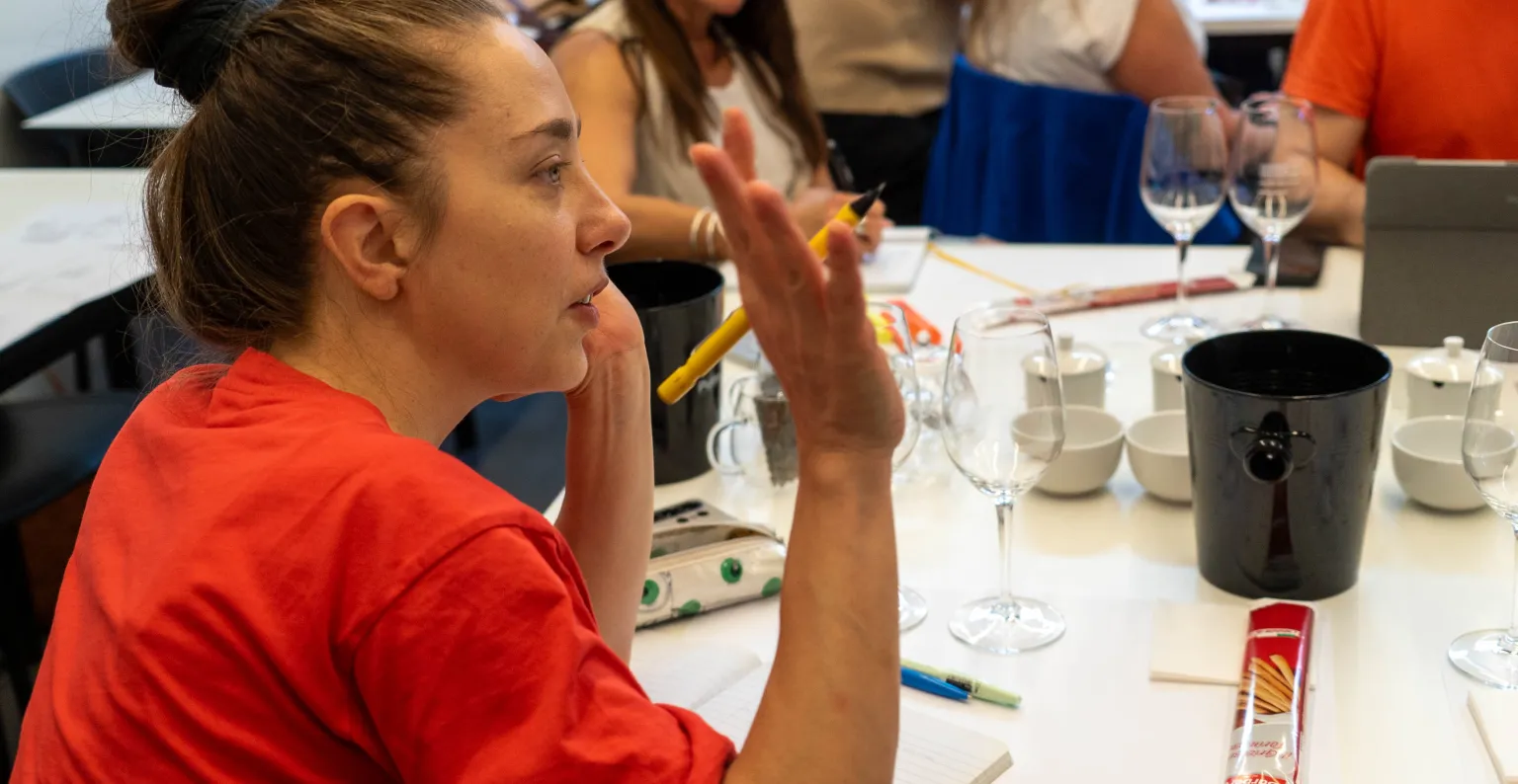 Una alumna levantando la mano para preguntar ante una mesa con instrumentos para vino