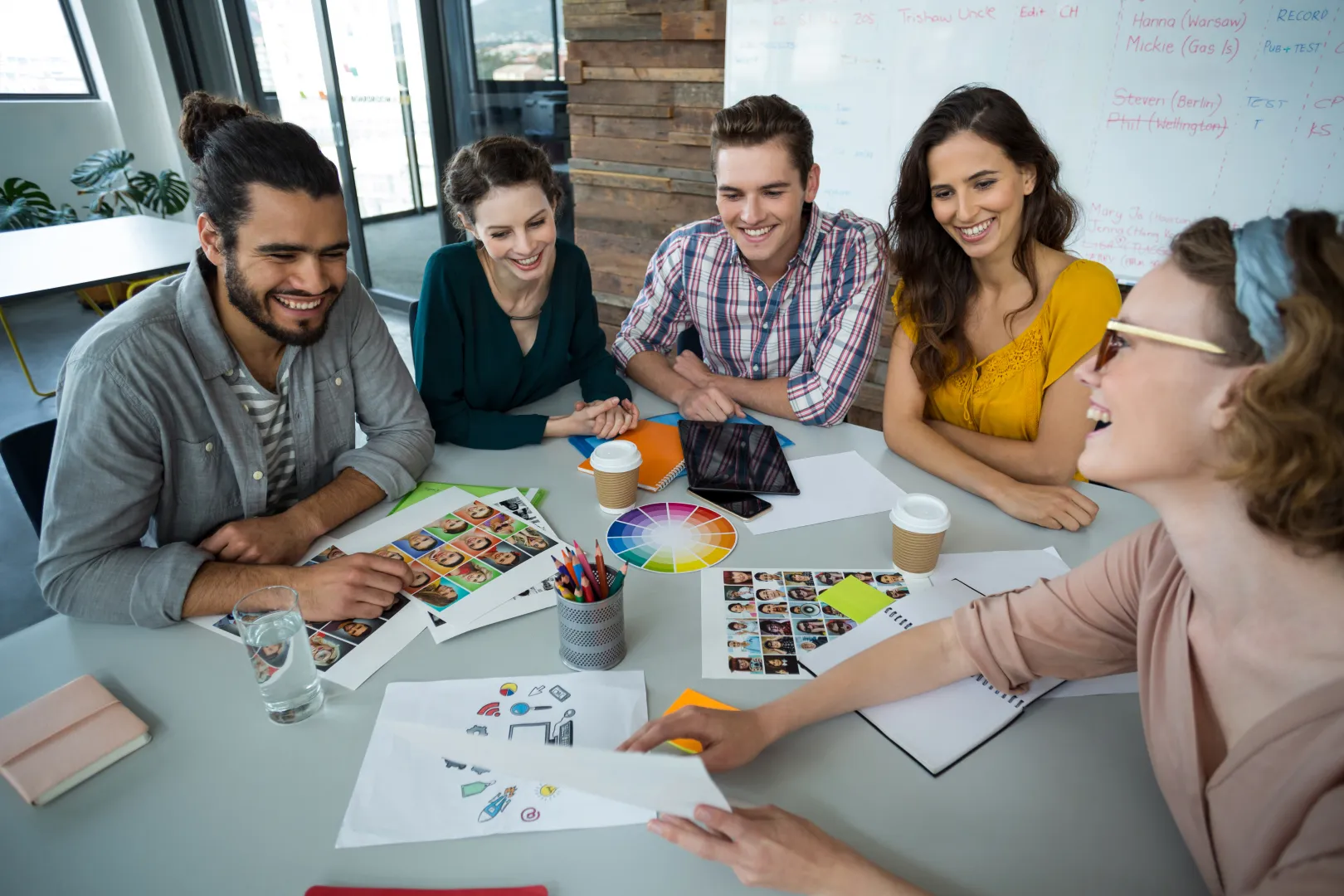 Equipo de diseñadores gráficos reunidos en una mesa colaborando en un proyecto creativo con paletas de colores, bocetos y fotografías.
